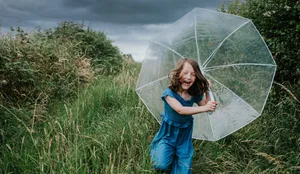A little girl runs towards the viewer, clutching an umbrella, as rainfall begins Selbstbewusstsein: Ein Mädchen mit einem Regenschirm