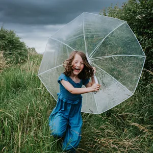 A little girl runs towards the viewer, clutching an umbrella, as rainfall begins Selbstbewusstsein: Ein Mädchen mit einem Regenschirm