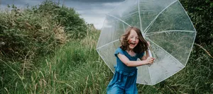 A little girl runs towards the viewer, clutching an umbrella, as rainfall begins Selbstbewusstsein: Ein Mädchen mit einem Regenschirm