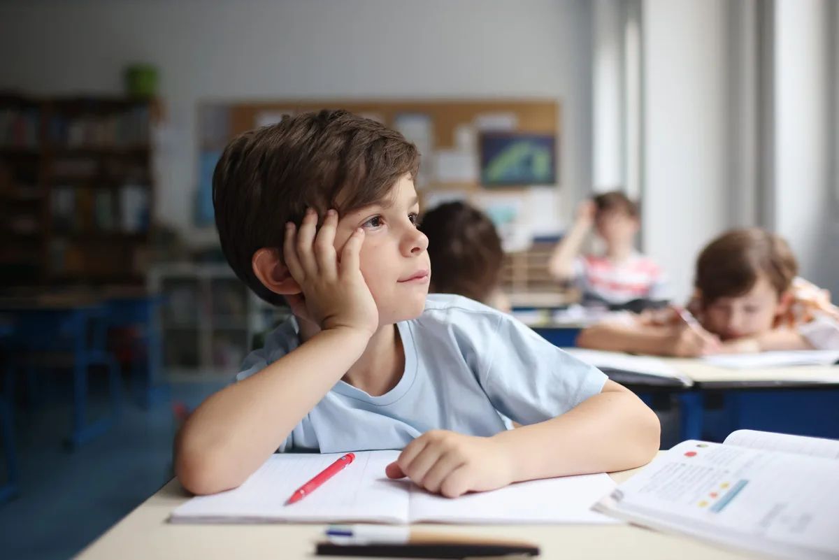 Un enfant qui rêve éveillé, regardant par la fenêtre d’une salle de classe Protection contre la chaleur : des élèves du primaire en classe