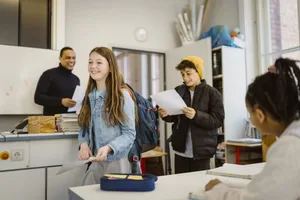 Des élèves, garçons et filles, souriants, marchant dans une salle de classe avec des documents à la main École : chaque enfant devrait avoir la possibilité de s'instruire