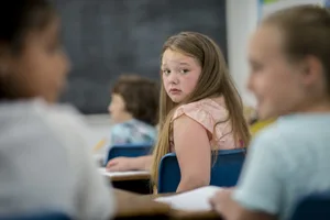 Bullismo a scuola: una ragazza guarda spaventata due compagne di classe che bisbigliano alle sue spalle Bullismo a scuola: una ragazza guarda spaventata due compagne di classe che bisbigliano alle sue spalle