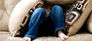 Header_Angsstörung_Kinder_Corona Ein Junge versteckt sich auf dem Sofa unter Kissen. Die Pandemie setzt Kindern und Jugendlichen besonders zu, sagt Kinder- und Jugendpsychiaterin Brigitte Contin-Waldvogel im Interview über Angststörungen und Corona.