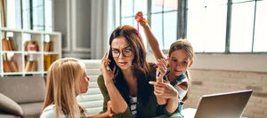 A business woman and a mother are trying to work on a laptop when her little daughters are playing, fooling around and interfering with her. Freelance, work from home. Alleinerziehende Mutter während Pandemie versucht mit zwei Kindern zu arbeiten