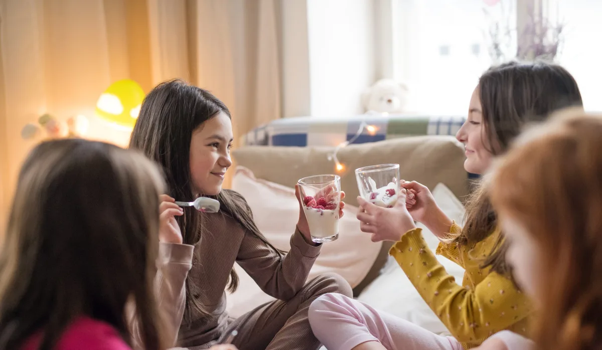 Group of small girl friends sitting on bed, eating. Übernachten: Freundinnen treffen sich zur Pijamaparty