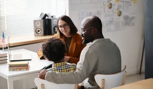 Un padre che parla con un insegnante in classe Un padre con il figlio e l'insegnante durante un colloquio con i genitori