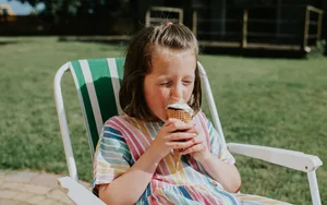 A young girl is eating an ice cream on a garden chair A young girl is eating an ice cream on a garden chair