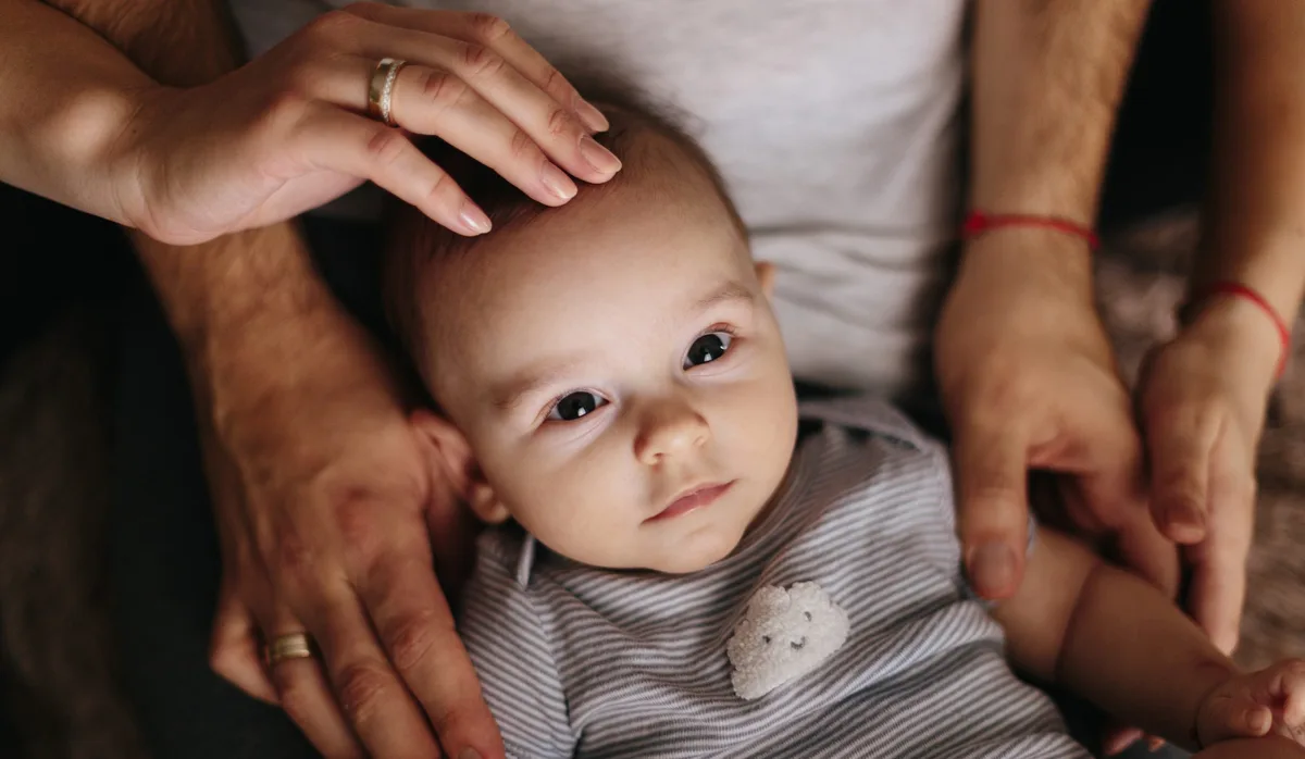 The lying baby in the hand of mother and father close-up. 4 months baby looking Seltene Krankheit, warten auf eine Diagnose: Baby wird von seinen Eltern gehalten