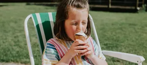 Junges Mädchen isst ein Glace auf dem Gartenstuhl Junges Mädchen isst ein Glace auf dem Gartenstuhl