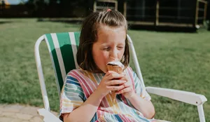 Junges Mädchen isst ein Glace auf dem Gartenstuhl Junges Mädchen isst ein Glace auf dem Gartenstuhl
