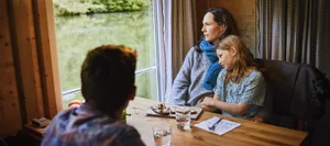 A relaxed family sitting at a table on a houseboat, eating bread and looking out of the window