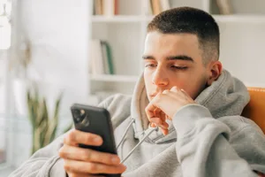 a young teenager at home looking at their mobile phone Mobile phones: A teenager talks about how he uses his