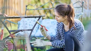 Donna che fa lavori di bricolage in giardino mentre vernicia un tavolo Scelta professionale: una giovane donna dipinge un tavolo da giardino