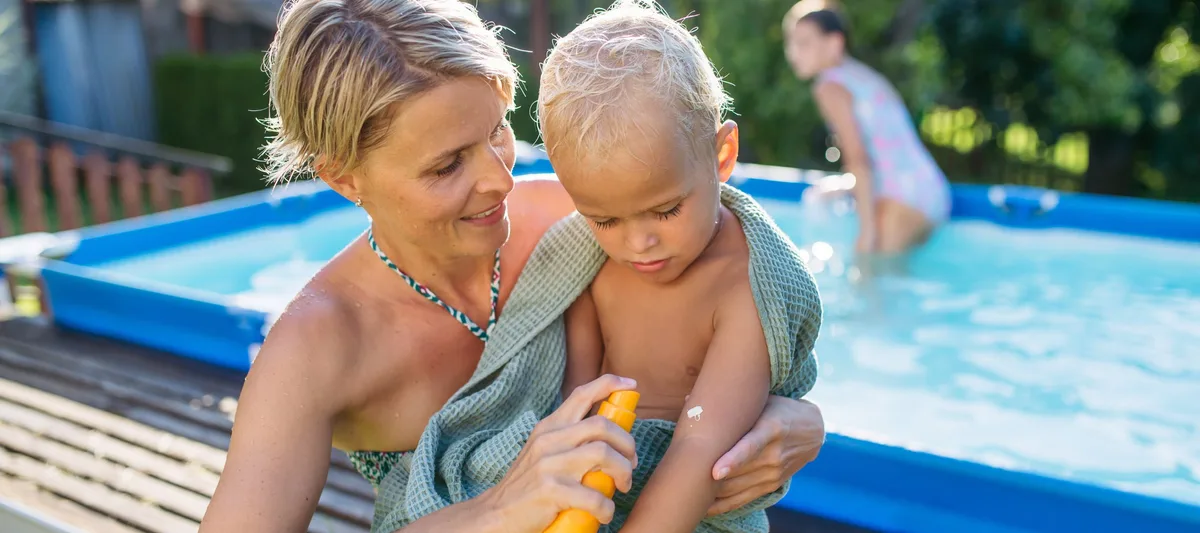 Mother applying sunscreen to toddler child near backyard pool on sunny summer day. Sonnencreme: Mutter cremt Kleinkind ein