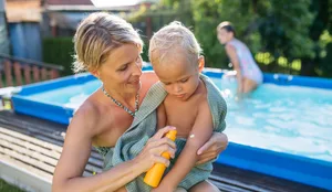 Mother applying sunscreen to toddler child near backyard pool on sunny summer day. Sonnencreme: Mutter cremt Kleinkind ein