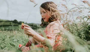 A little girl sits on long grass on a summers day, picking buttercups Allergien bei Kindern nehmen zu: Ein Mädchen sitzt in einem Feld.