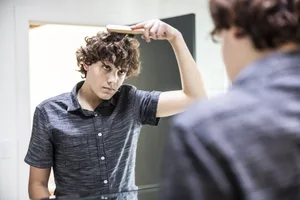 A teenage boy brushing his hair in the bathroom mirror Puberty: Teenager brushes their hair in front of the bathroom mirror