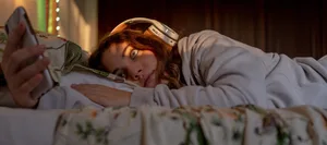 26-10-cyberbullying-Swisscom-Swiss-Parents’ Magazine-ed A girl is lying in bed with her headphones on and her smartphone