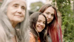Portrait of smiling woman sitting with daughter and mother in backyard Prägung: 3 Generationen Frauen