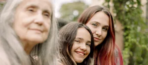 Portrait of smiling woman sitting with daughter and mother in backyard Prägung: 3 Generationen Frauen