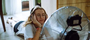 Sonic oasis: A teen girl creates her personal oasis on the floor, listening to music through wireless headphones in front of a cooling fan Klimawandel: Teenagermädchen mit Kopfhörern vor Ventilator