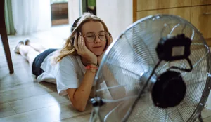 Sonic oasis: A teen girl creates her personal oasis on the floor, listening to music through wireless headphones in front of a cooling fan Klimawandel: Teenagermädchen mit Kopfhörern vor Ventilator