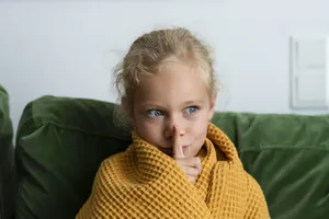 Jeune fille pensive, enveloppée dans une couverture, faisant un geste de silence chez elle Les enfants hypersensibles sont souvent plus sensibles au bruit