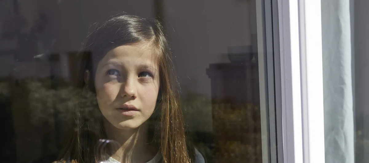 Einzelkind im Lockdown Verträumte Kinder: Ein Mädchen blickt durch ein Glasfenster.