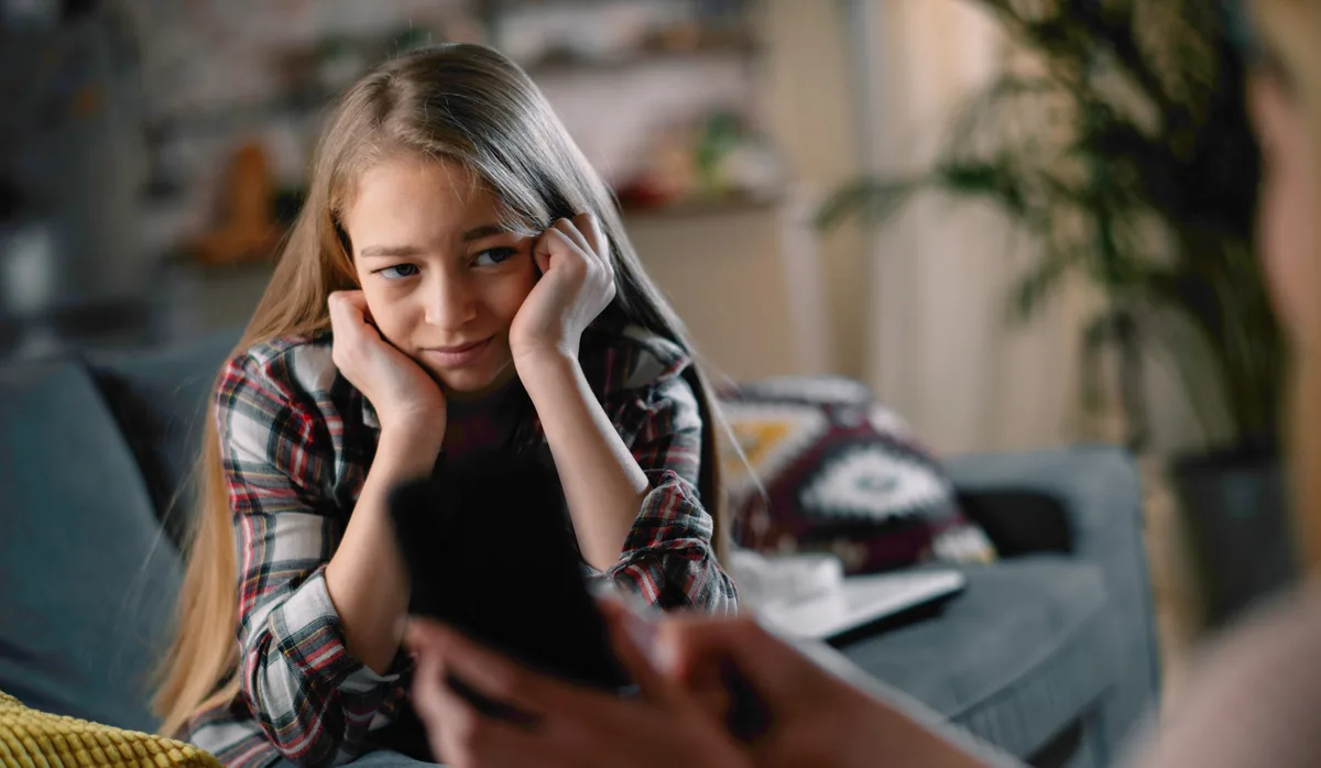 Eine Jugendliche sitzt frustriert auf dem Sofa, wird von der Mutter ermahnt. Eine Jugendliche sitzt frustriert auf dem Sofa, wird von der Mutter ermahnt.