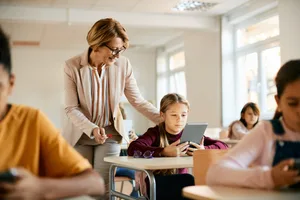 Un enseignant aide une élève à utiliser une tablette numérique pendant un cours à l’école. Une enseignante dans sa classe