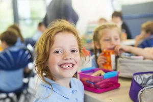Une fillette souriante à qui il manque une dent, en train de manger un déjeuner équilibré TDAH et alimentation : les filles qui prennent une collation à l'école