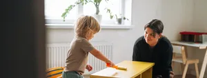 Mother and toddler painting a wooden cabinet with yellow paint at home, DIY renovation with kids concept Trennung: Kind mal ein Holmöbel an und Mutter sitzt daneben