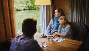 Une famille détendue, assise à table sur une péniche, un morceau de pain à la main, regardant par la fenêtre