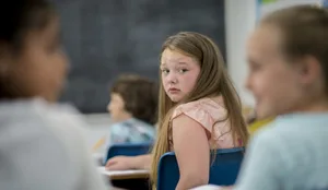 Mobbing in der Schule: Ein Mädchen schaut ängstlich nach hinten zu 2 tuschelnden Klassenkameradinnen Mobbing in der Schule: Ein Mädchen schaut ängstlich nach hinten zu 2 tuschelnden Klassenkameradinnen
