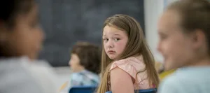Mobbing in der Schule: Ein Mädchen schaut ängstlich nach hinten zu 2 tuschelnden Klassenkameradinnen Mobbing in der Schule: Ein Mädchen schaut ängstlich nach hinten zu 2 tuschelnden Klassenkameradinnen
