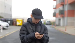 Male pedestrian concentrating on smartphone amidst cityscape under gray sky Männlicher Teenager am Smartphone