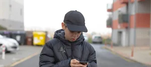 Male pedestrian concentrating on smartphone amidst cityscape under gray sky Männlicher Teenager am Smartphone