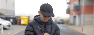 Male pedestrian concentrating on smartphone amidst cityscape under gray sky Männlicher Teenager am Smartphone