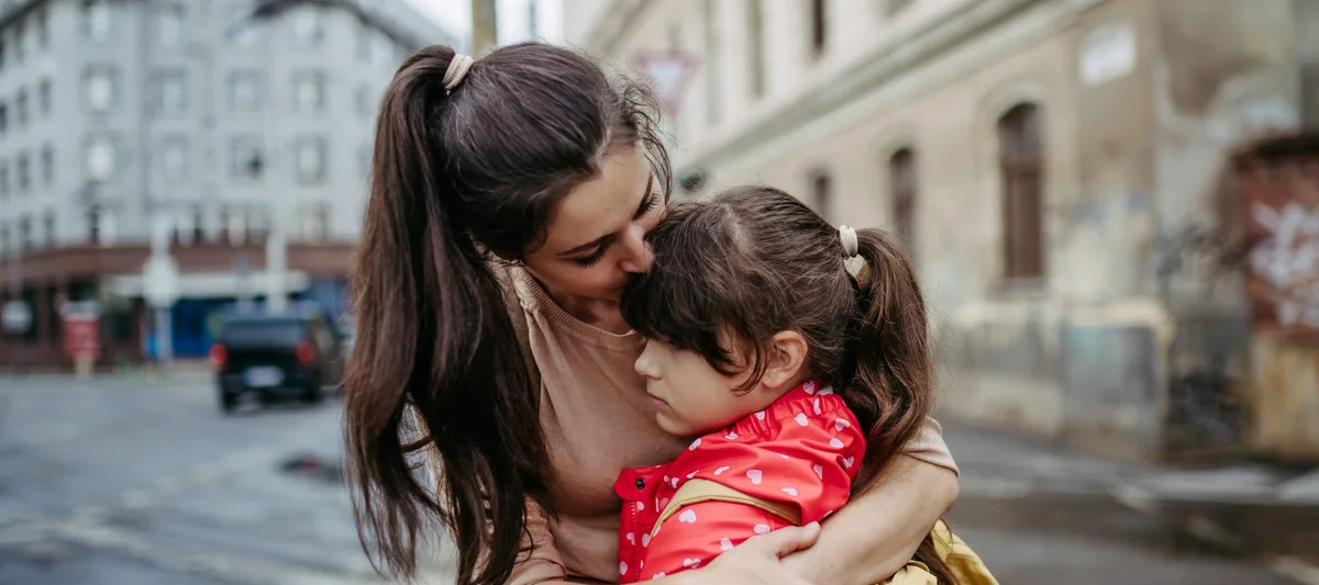 Mother hugging daughter on a city street. Young girl with anxiety doesn’t want to go to school. Fear of bullying. Empathie: Eine Mutter tröstet ihre Tochter