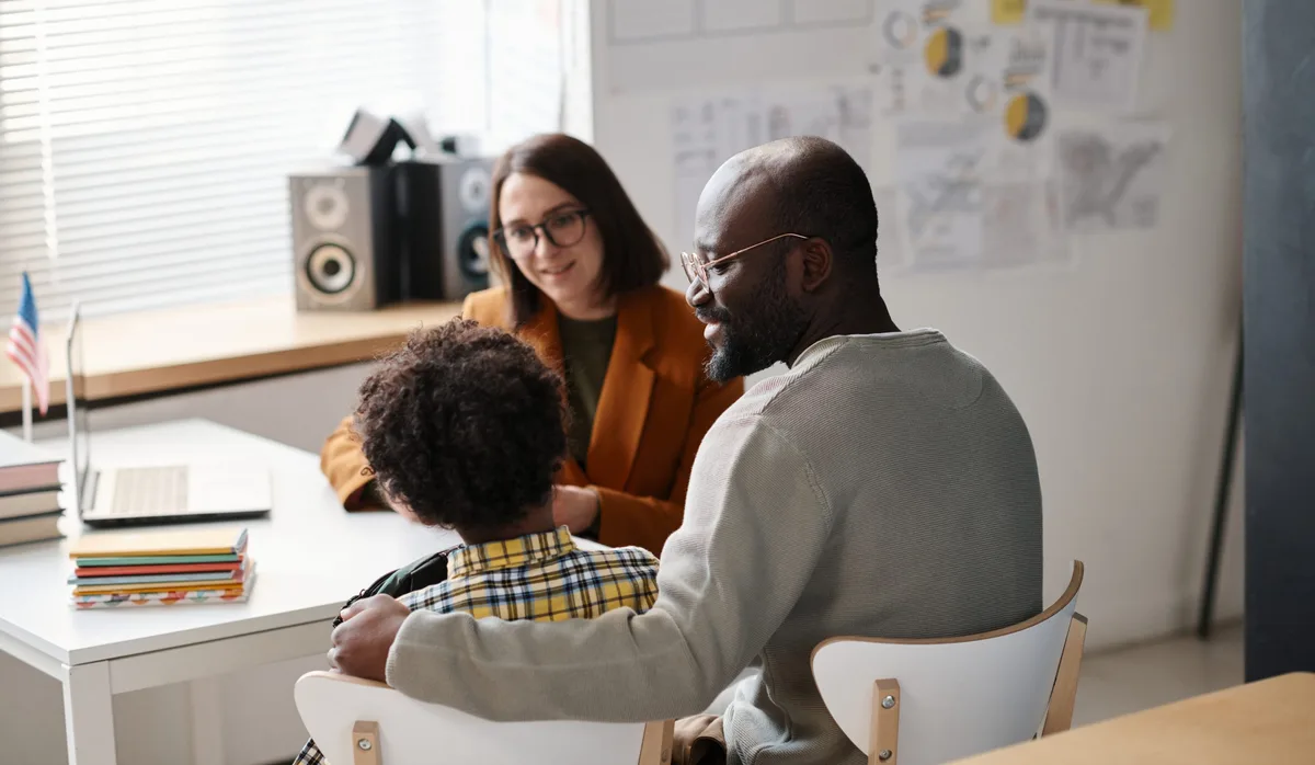 Father talking to teacher in classroom Vater mit Sohn und Lehrerin beim Elterngespräche