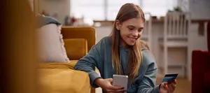 Una ragazza felice che effettua un pagamento online con la sua carta di credito e il cellulare. La prima ricompensa: una ragazza con la sua carta di credito
