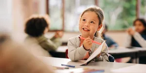 Jeune fille en train de dessiner dans une salle de classe à la rentrée scolaire Apprendre avec motivation : une fillette est assise dans la salle de classe, tout enthousiaste