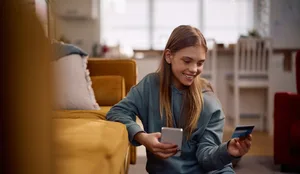 Happy teenager paying online with her credit card and cell phone. Der erste Lohn: Eine Jugendliche mit ihrer Kreditkarte