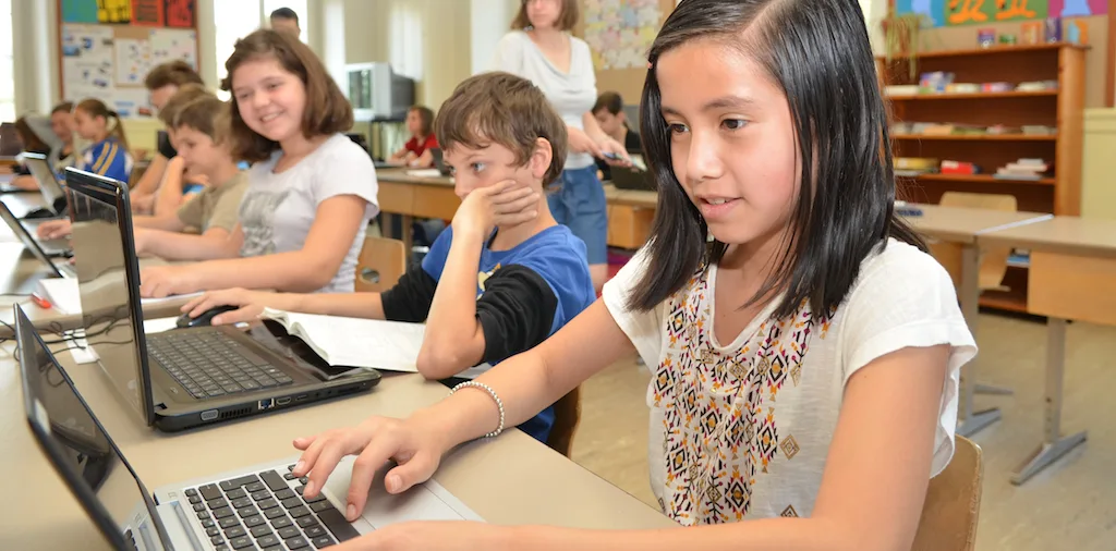 Header_Sch_ler_programmieren Kinder lernen zu programmieren: Ein Mädchen schaut konzentriert auf den Bildschirm, neben ihr sitzen ihre Mitschüler und machen dasselbe.