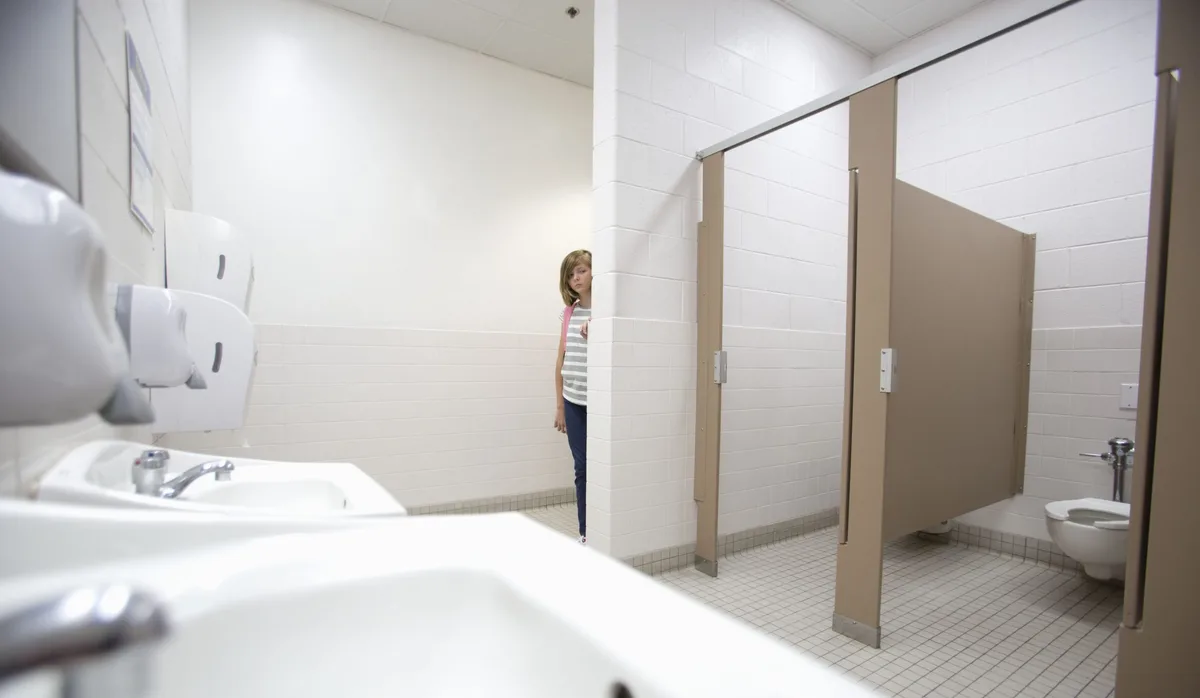 School Girl Ein Kind schaut vorsichtig um die Ecke einer Schultoilette