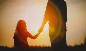 silhouette of little girl holding parent hand at sunset Kosmos Kind