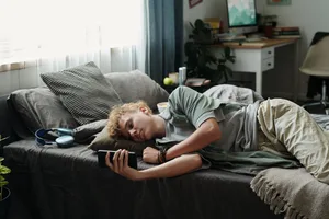 Un adolescent caucasien allongé sur son lit, utilisant son smartphone et souffrant d’une dépendance aux gadgets Réseaux sociaux : un garçon est allongé sur son lit, son téléphone portable à la main