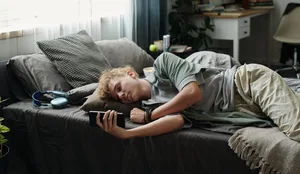 Teenage Caucasian Boy Lying on Bed Using Smartphone Suffering Gadget Addiction Social Media: Ein Junge liegt mit dem Handy auf dem Bett