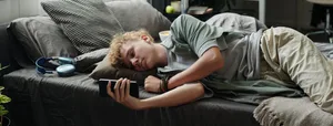 Teenage Caucasian Boy Lying on Bed Using Smartphone Suffering Gadget Addiction Social Media: Ein Junge liegt mit dem Handy auf dem Bett