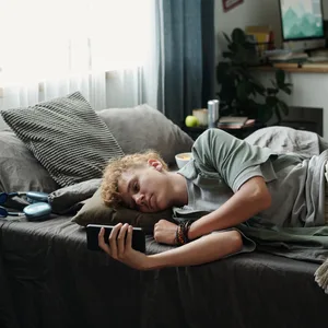 Teenage Caucasian Boy Lying on Bed Using Smartphone Suffering Gadget Addiction Social Media: Ein Junge liegt mit dem Handy auf dem Bett
